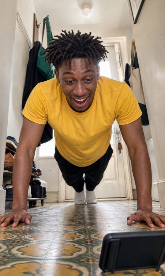 Mal laughing during a phone-counted push-up set in a narrow hallway
